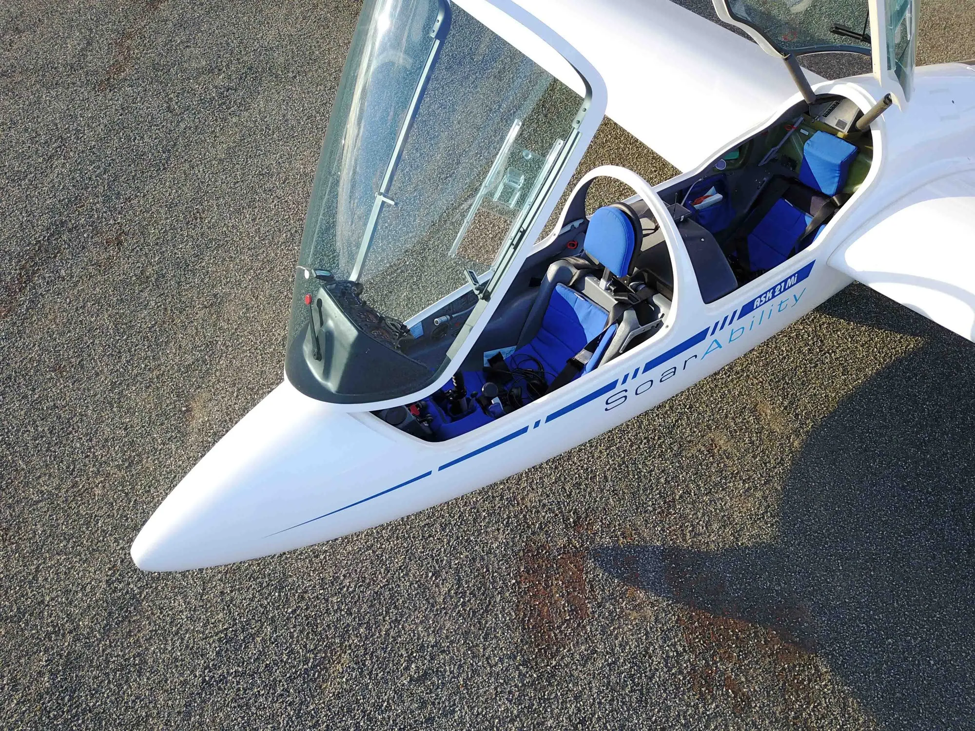 The nose and open canopy of SoarAbility's ASK21Mi on the gravel apron at Cunderdin, hand controls visible in both cockpits