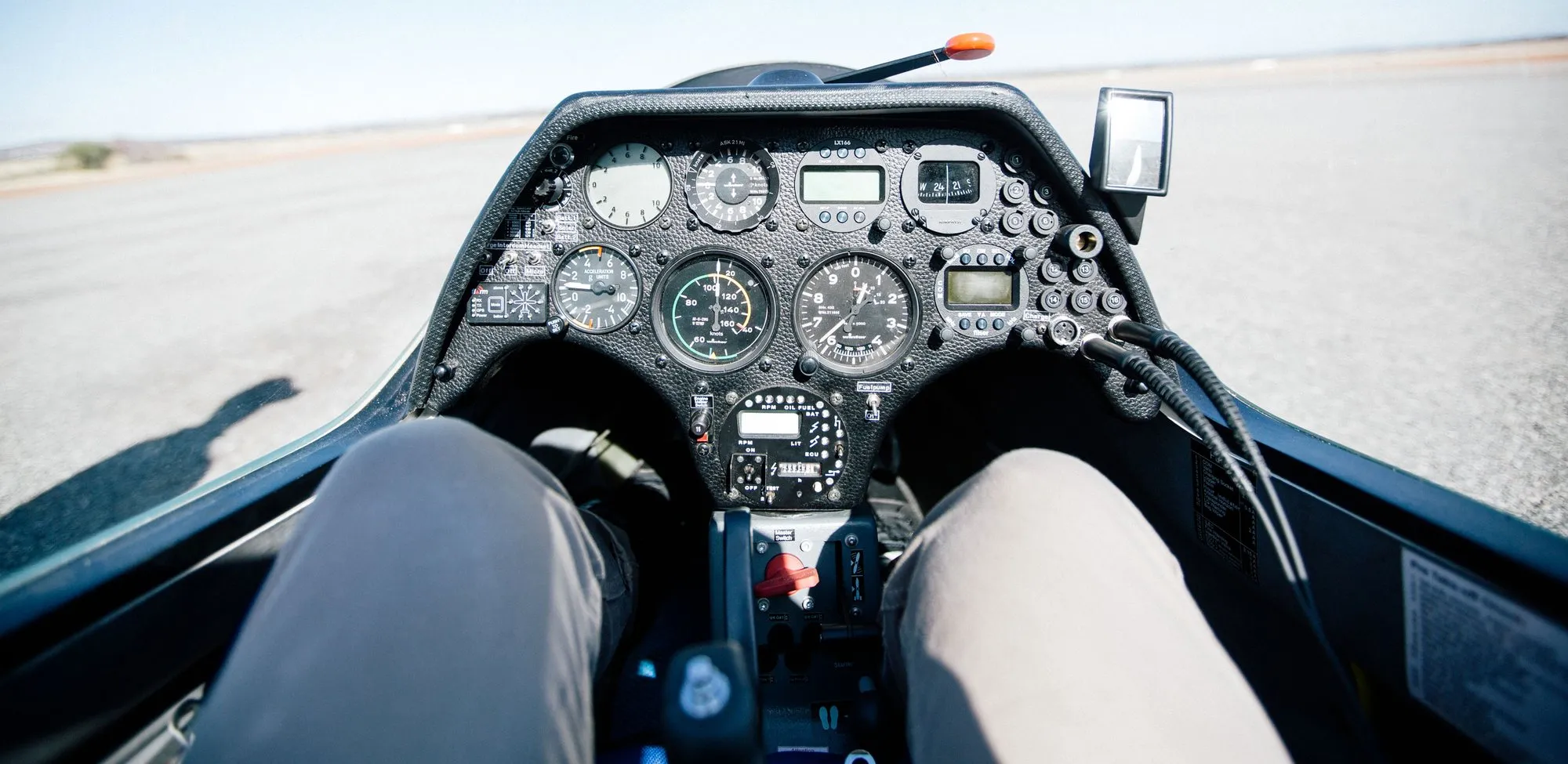 View from the glider's front seat in flight: instrument panel, the pilot's legs, and salt-lake country far below